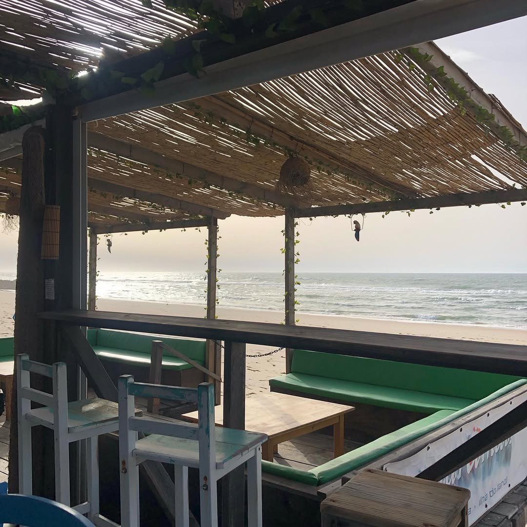 Esplanada coberta de canas, com bancos e mesas virados para o mar